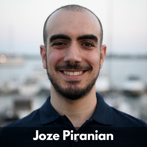 Joze Piranian is a Canadian man of Middle-eastern descent in his 30s. He has close cropped dark hair with a short beard and moustache. He wears a dark button up shirt.